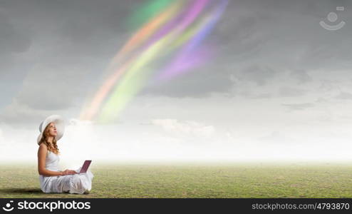 Lady using laptop. Young lady sitting on green grass with laptop on knees