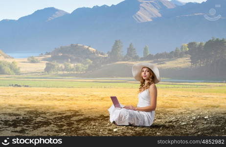 Lady using laptop. Young lady sitting on green grass with laptop on knees