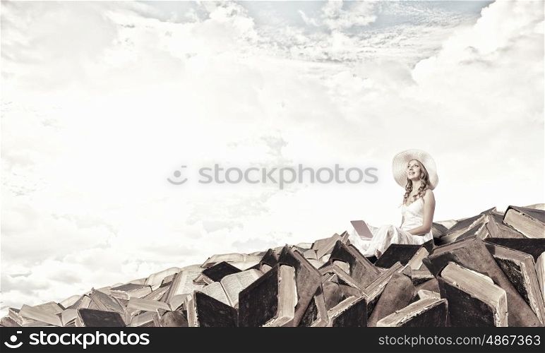 Lady using laptop. Young lady sitting on pile of books with laptop