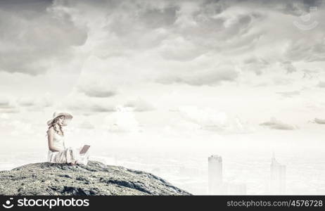 Lady using laptop. Young lady sitting on top of mountain with laptop