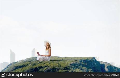 Lady using laptop. Young lady sitting on top of mountain with laptop