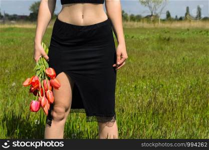lady with a bouquet of tulips, view of the legs and torso. Young woman with a bouquet of tulips in the field.. lady with a bouquet of tulips, view of the legs and torso.