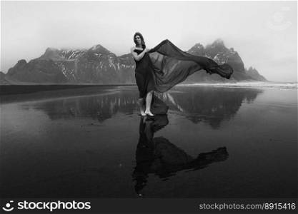 Lady with long chiffon cape on sea beach monochrome scenic photography. Picture of person with hills on background. High quality wallpaper. Photo concept for ads, travel blog, magazine, article. Lady with long chiffon cape on sea beach monochrome scenic photography