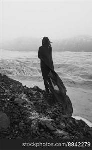 Lady wrapped with gentle fabric on cliff monochrome scenic photography. Picture of person with old glacier on background. High quality wallpaper. Photo concept for ads, travel blog, magazine, article. Lady wrapped with gentle fabric on cliff monochrome scenic photography