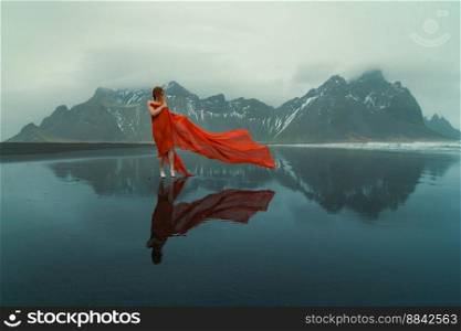 Lady wrapped with red fabric on Reynisfjara beach scenic photography. Picture of person with hills on background. High quality wallpaper. Photo concept for ads, travel blog, magazine, article. Lady wrapped with red fabric on Reynisfjara beach scenic photography