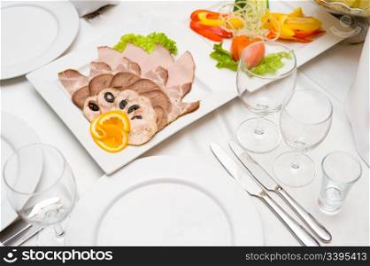 laid table with tableware and cold snacks for banquet, focus at orange on meat assortment