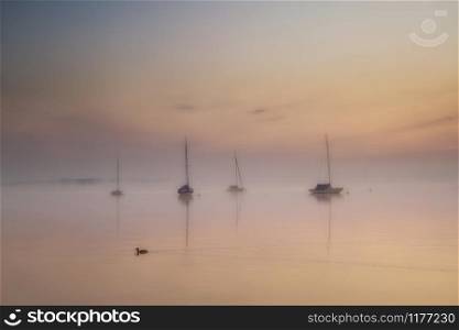 lake Ammersee in Bavaria at a foggy sunrise with sailboats