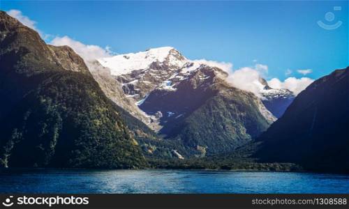 Lake and mountain landscape with snow capped peak under summer sunlight in blue sky background. Shot in Milford Sound, Fiordland National Park, South Island of New Zealand.