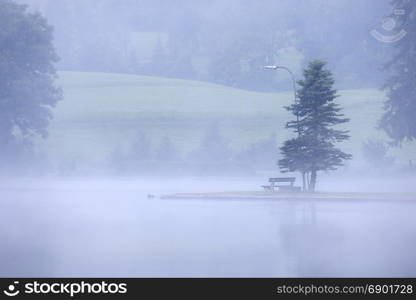 Lake at foggy morning misty weather. Alpine mountain park