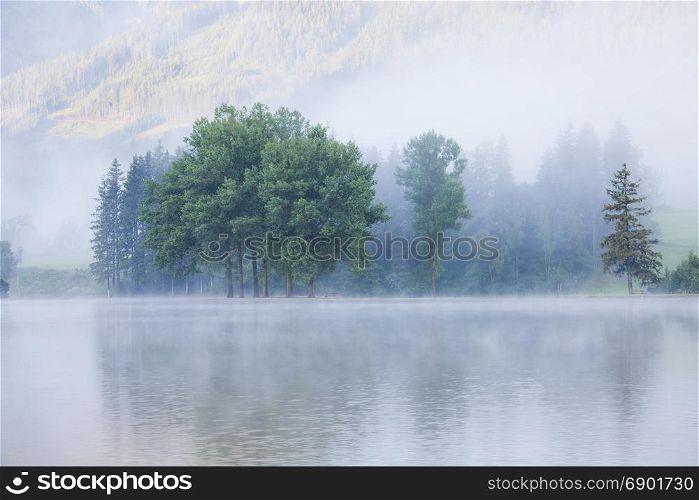 Lake at foggy morning misty weather. Alpine mountain park