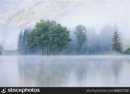 Lake at foggy morning misty weather. Alpine mountain park
