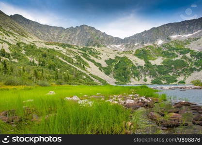 Lake at foot of mountain range. River in mountain valley along rocks. Summer morning in mountains of Siberia