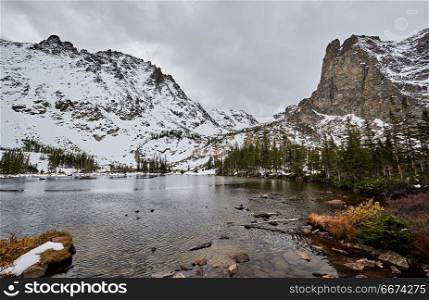 Lake Helene, Rocky Mountains, Colorado, USA. . Lake Helene with rocks and mountains in snow around at autumn with cloudy sky. Rocky Mountain National Park in Colorado, USA.