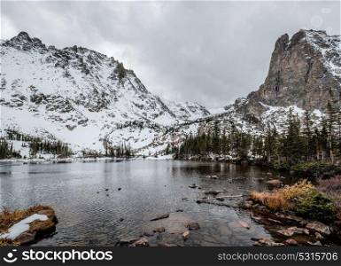 Lake Helene with rocks and mountains in snow around at autumn with cloudy sky. Rocky Mountain National Park in Colorado, USA.