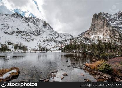 Lake Helene with rocks and mountains in snow around at autumn with cloudy sky. Rocky Mountain National Park in Colorado, USA.