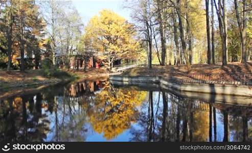 lake in beautiful autumn city park, behind trees wooden house