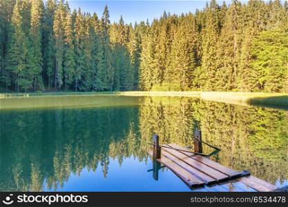Lake in the forest with blue water and wooden bridge. Forest lake in the mountains