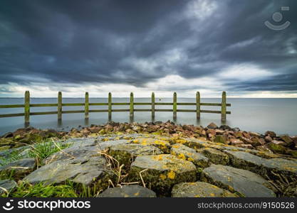 Lake view at dark time with heavy clouds and stormy winds. Stretch dam in the lake with a wooden pile construction