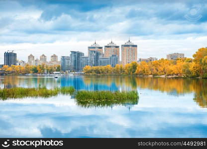 Lake with blue water, autumn yellow forest and high buildings on other bank