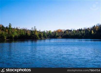Lake with ripples against reflected forest and clear blue sky.