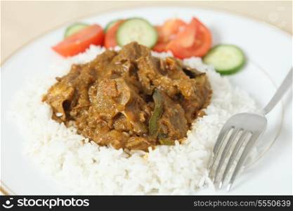Lamb rogan josh, with basmati rice and a salad of tomato and cucumber. The lamb, on the bone is in a spicy tomato sauce.