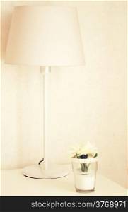 Lamp and flower on the table near bed with retro filter effect