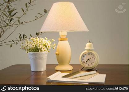 Lamp on a table with a plant, clock and notebook and pen