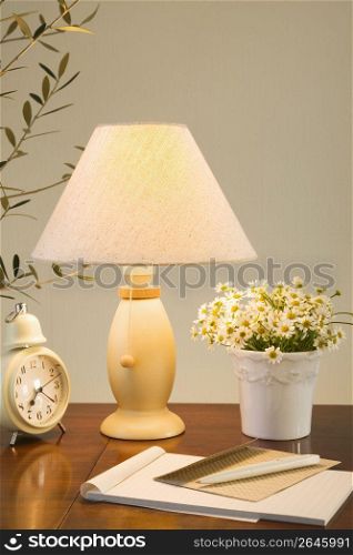 Lamp on a table with a plant, clock and notebook and pen