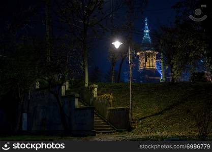 Lamp post illuminating some stairs and a church in the background. Night scene
