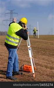 Land surveyors measuring land with theodolite speaking through transmitter