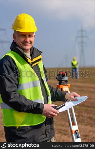 Land surveyors measuring with tacheometer hold construction plans on site