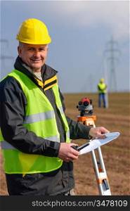 Land surveyors measuring with tacheometer hold construction plans on site