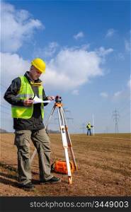 Land surveyors measuring with tacheometer looking at plan construction site