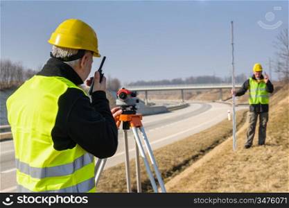 Land surveyors measuring with tacheometer speaking through transmitter highway
