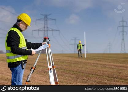 Land surveyors on construction site reading plans wear reflective clothing
