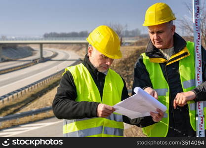 Land surveyors on highway reading geodesist plans use tacheometer