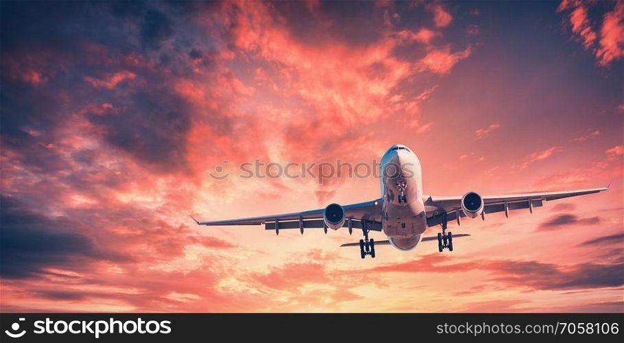 Landing airplane against colorful sky at sunset. Landscape with aircraft is flying in the red sky with multicolored clouds. Travel background with passenger plane. Commercial airplane. Private jet