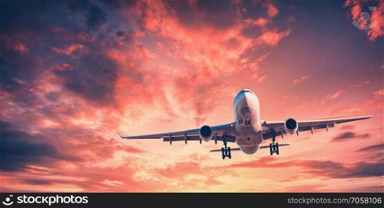 Landing airplane against colorful sky at sunset. Landscape with aircraft is flying in the red sky with multicolored clouds. Travel background with passenger plane. Commercial airplane. Private jet