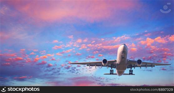 Landing airplane. Landscape with white passenger airplane is flying in the blue sky with pink clouds at sunset. Travel background. Passenger airliner. Business trip. Commercial aircraft. Private jet