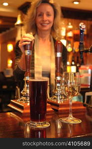 landlady standing behind bar with drinks on bar top