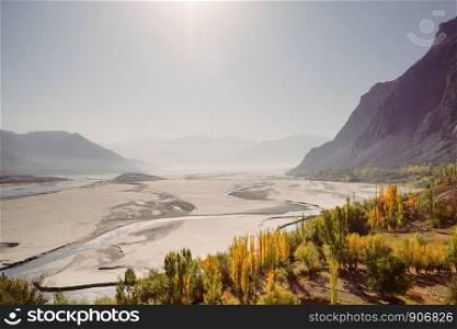 Landscape aerial view of Indus river flowing through Katpana cold desert in Skardu with misty mountain range in the background. Beautiful foliage in autumn season. Gilgit Baltistan, Pakistan.