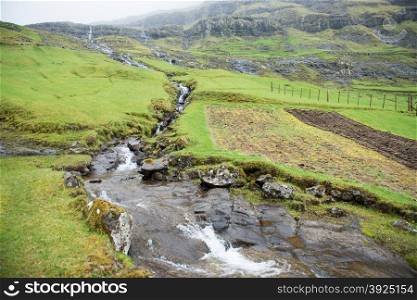 Landscape around Tjornuvik on the Faroe Islands with waterfall and green grass