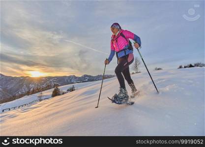 Landscape at sunset in the mountains with girl running downhill with snowshoes