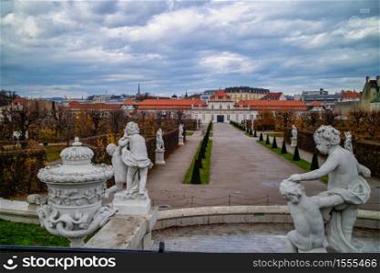 Landscape before Unteres Belvedere with marble ancient statues and sculptures on a forefront on a background of cloudy autumn grey sky in Vienna, Austria .. Marble statues in baroque style before Schloss Belvedere in Vienne.