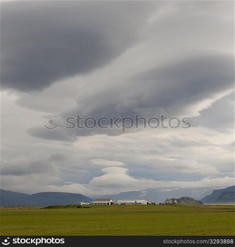 Landscape, cloudy sky over farmyard and distant mountain
