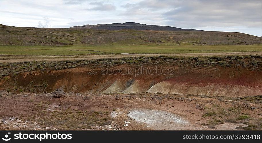 Landscape, eroded mineral rich gully through grassland, before grassy mountains