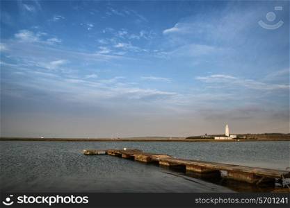 Landscape image large sky with jetty and lake with lighthouse in distance