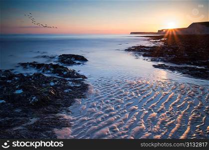 Landscape image of rocky beach at susnet with long exposure motion blur sea
