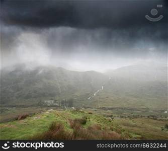 Landscape image of storm clouds hanging over Snowdonia mountain range with heavy rainfall in Autumn with misty weather