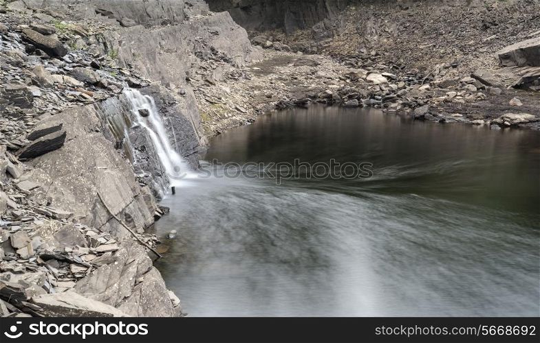 Landscape image of waterfall flowing into old abandoned quarry